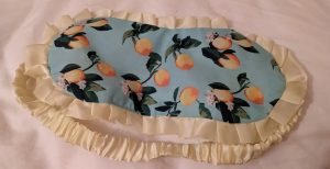 Frilly yellow edged sleep mask with lemons and their leaves on a blue background. Yellow elastic strap for securing it around your head.