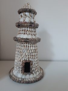 A photo of my lighthouse decorated with shells. There is a rectangular gap at the bottom that is designed to look like the door.