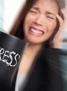 A lady nearly in tears grimacing with her hand held to the side of her head. Holding a black mug in the other hand with stress written on it in white writing