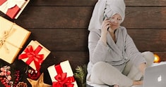 A lady in her pyjamas with her hair wrapped in a towel sitting next to Christmas presents whilst on the phone