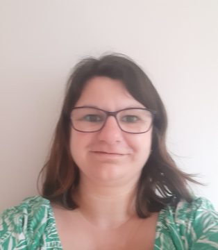 Emily Arlidge, owner of The Lighthouse Counselling. White female wearing purple glasses, shoulder length brown hair and a green and white dress showing only her shoulders.