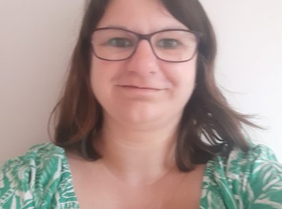 Emily Arlidge, owner of The Lighthouse Counselling. White female wearing purple glasses, shoulder length brown hair and a green and white dress showing only her shoulders.